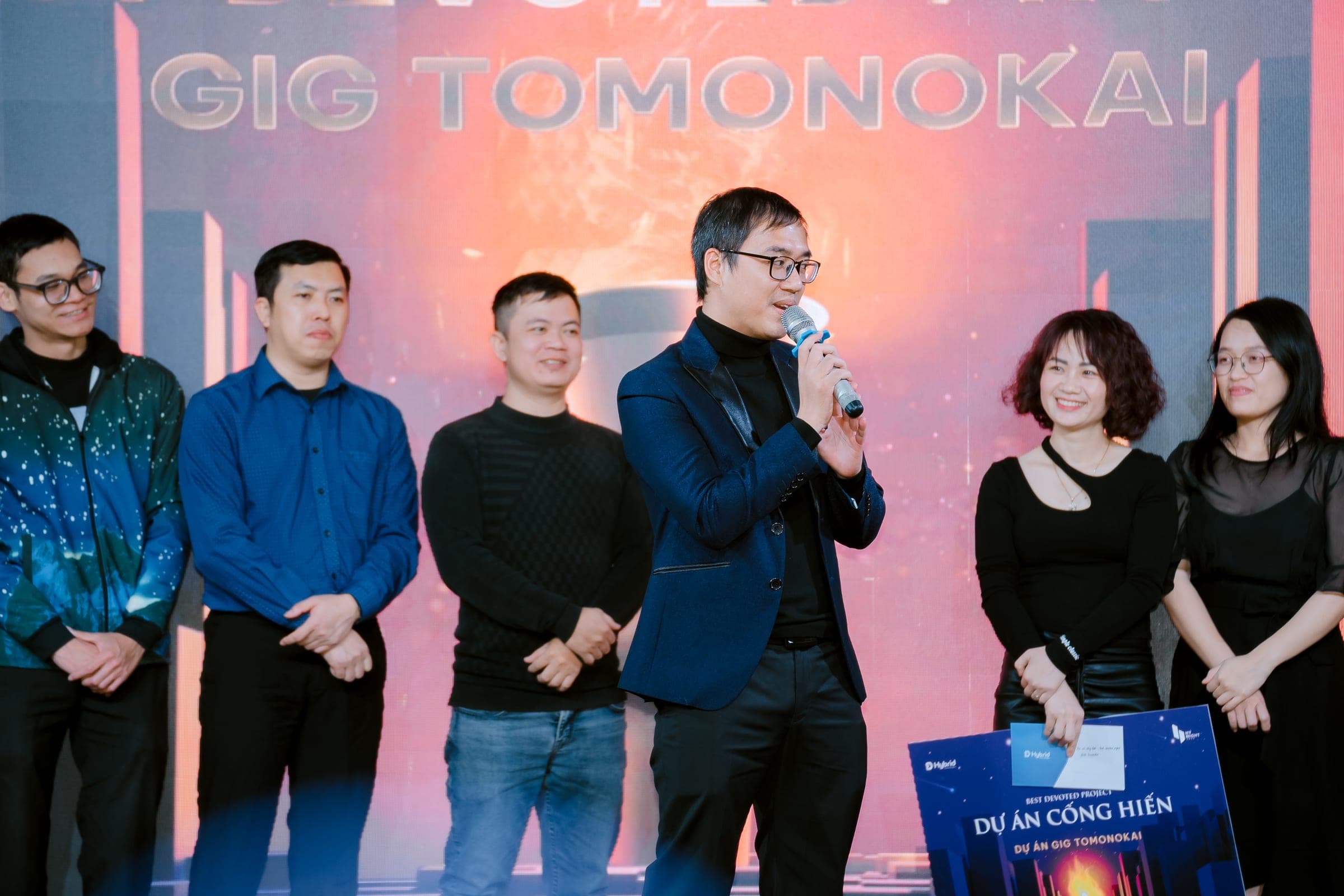 Chien Le speaking on stage as his team receives the best devoted project award for GIG Tomonokai